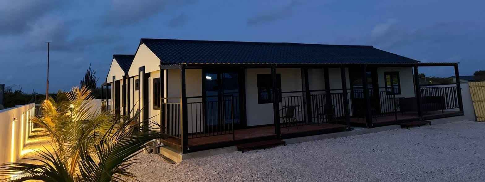MZ ECO modular house at dusk with a lit covered porch, dark tiled roof and gravel yard