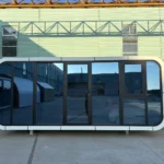A30 white apple cabin with black-framed panoramic glazing in the factory yard