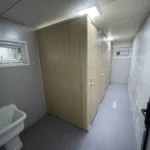 Public restroom apple cabin interior with wood-look cubicle doors and a corridor