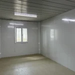Open interior of the cream-panel detachable container house with paneled walls and an unfinished floor