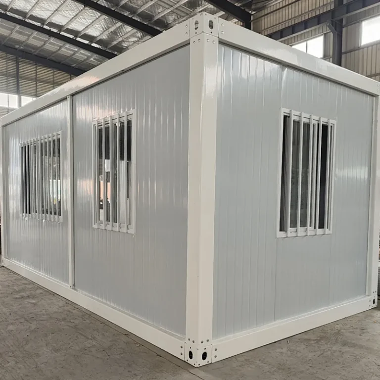 White detachable container house with barred windows on two adjacent walls inside a factory
