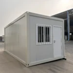 White detachable container house with an end-wall door, barred window and plain side wall