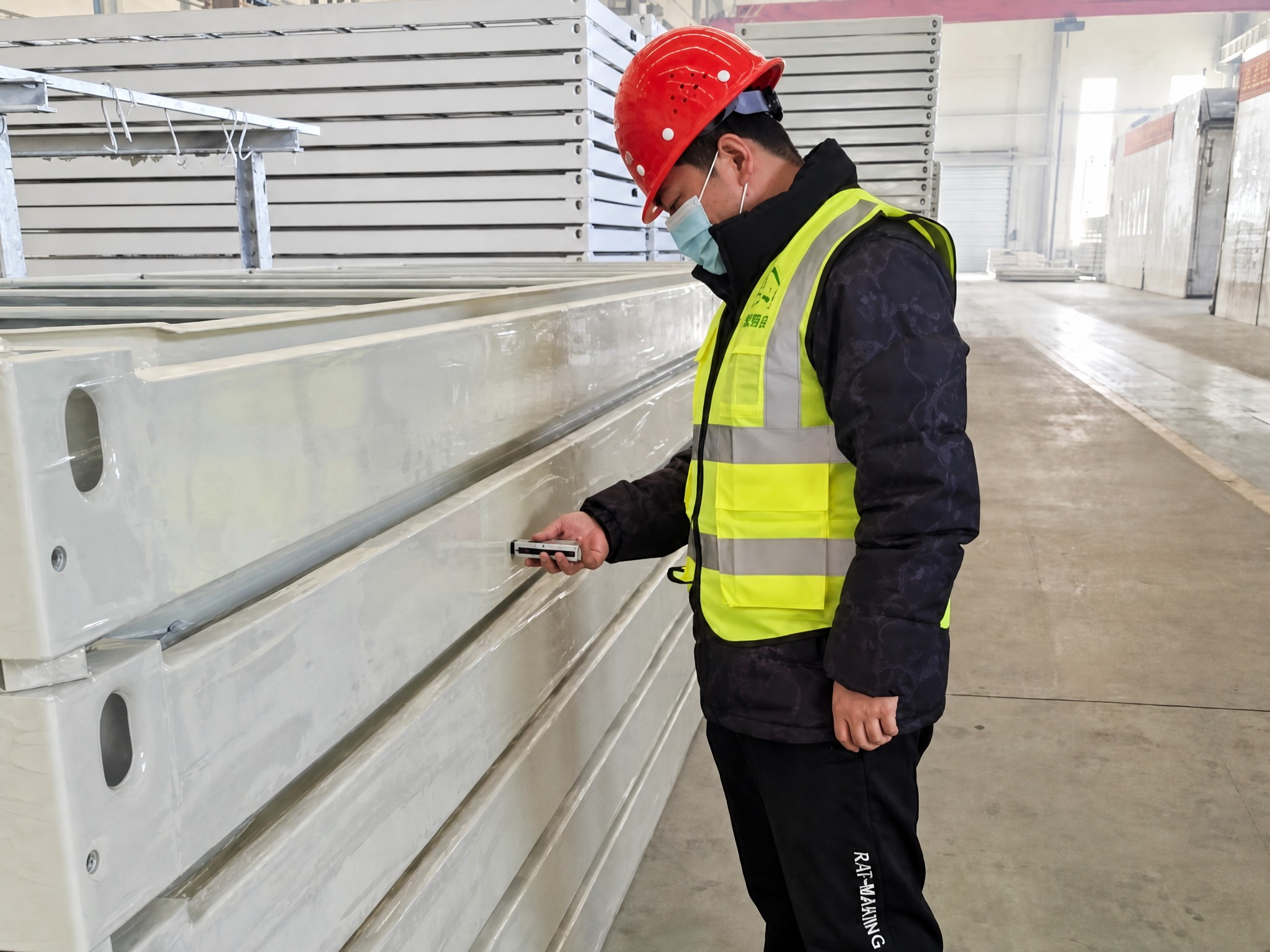 Worker in hi-vis vest and red helmet measuring an MZ ECO insulated panel during inspection