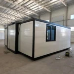 Side and rear of a white expandable container house with black framing and a sliding window