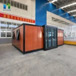 Wood-look expandable container house with black framing and a central glazed entrance inside the factory