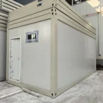Beige flat pack toilet unit with an entrance door and a small window