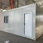 Light-coloured flat pack container house with a side entrance and barred windows