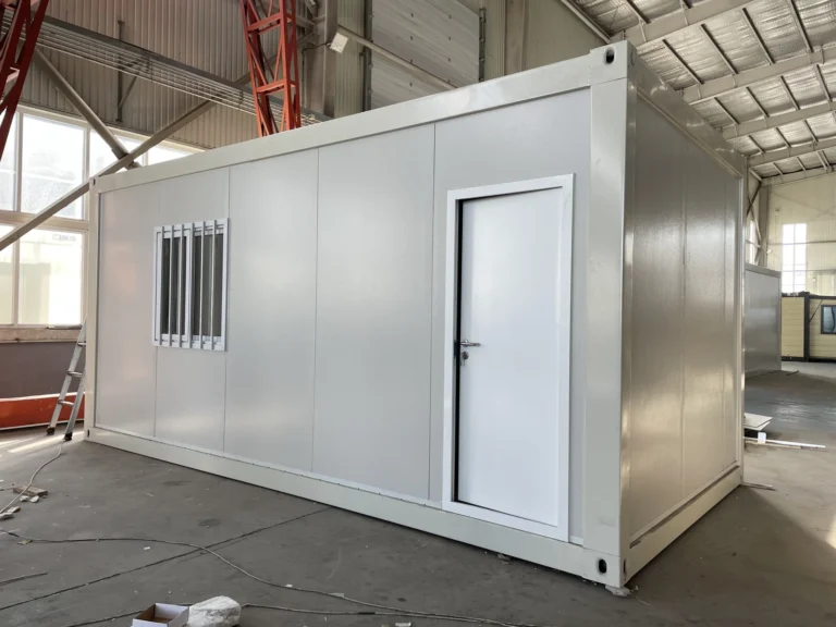Light-coloured flat pack container house with a side entrance and barred windows