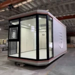Compact assembled capsule with light wall panels and dark corner glazing inside the factory