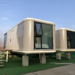 White and grey G60S space capsule house with broad end glazing on a green display platform