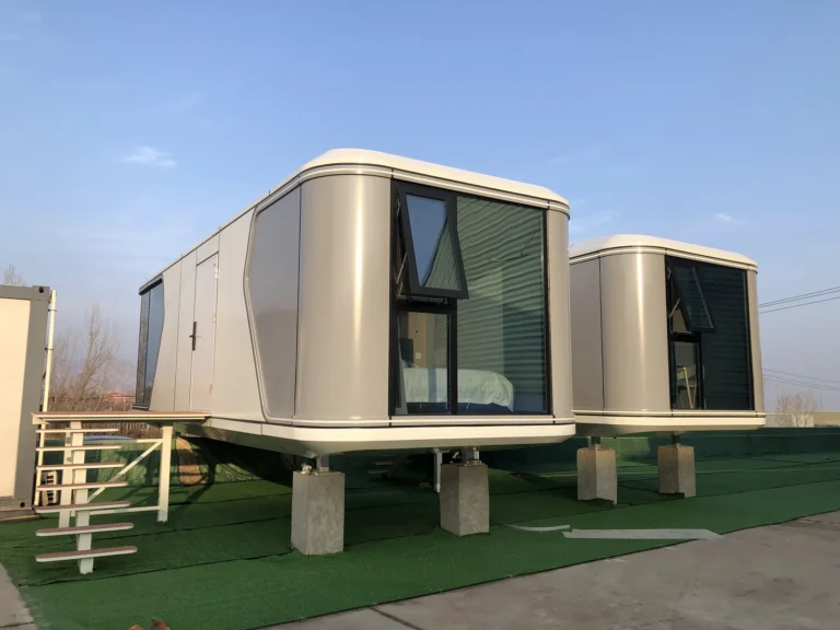 White and grey G60S space capsule house with broad end glazing on a green display platform