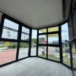 Unfurnished capsule interior with wood-look flooring and dark-framed panoramic windows