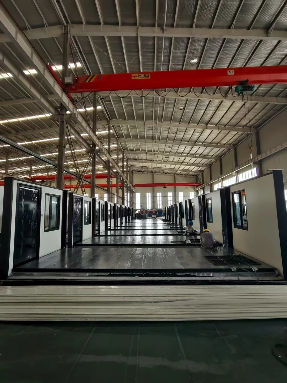 Container house manufacturing line beneath a red overhead crane
