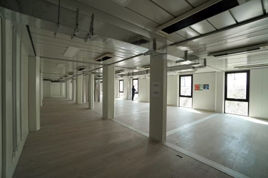 Modular unit interior showing a long corridor with side doors, ceiling lights and daylight from the end window
