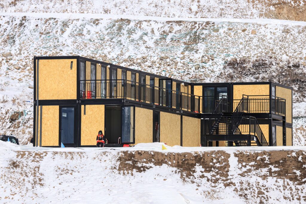 Stackable container module building in two storeys with black steel frames and gold panels, assembled from stacked units