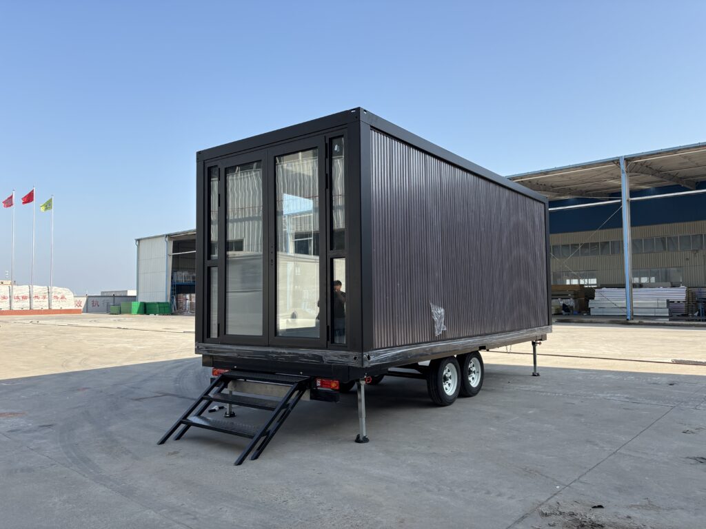 Charcoal-grey Z-type container house on a tandem-axle trailer, with full-height glazed doors and steps at the entrance
