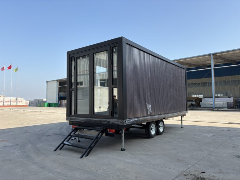 Charcoal-grey Z-type container house on a tandem-axle trailer, with full-height glazed doors and steps at the entrance